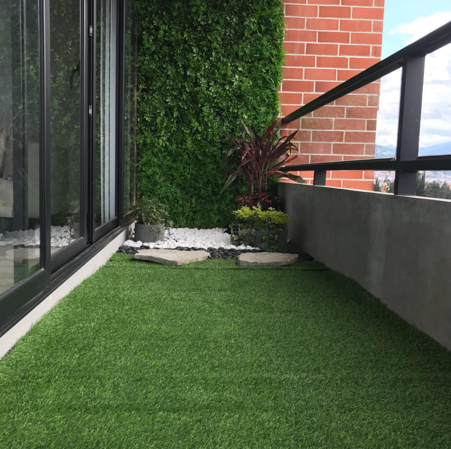 Balcón con césped sintético, pared verde y sendero de piedra