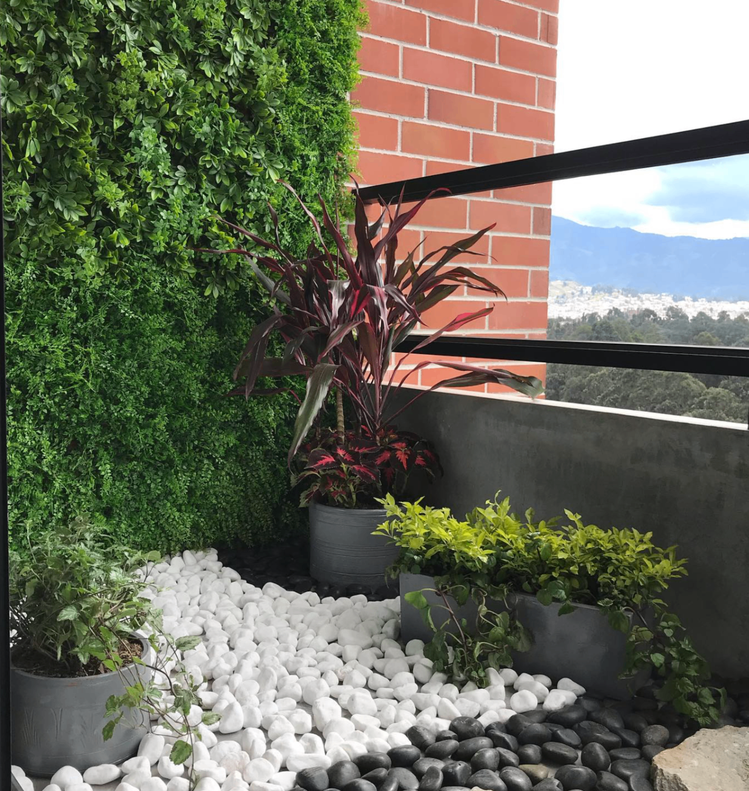 Balcón con pared verde, piedras blancas y macetas decorativas con vista a Cuenca