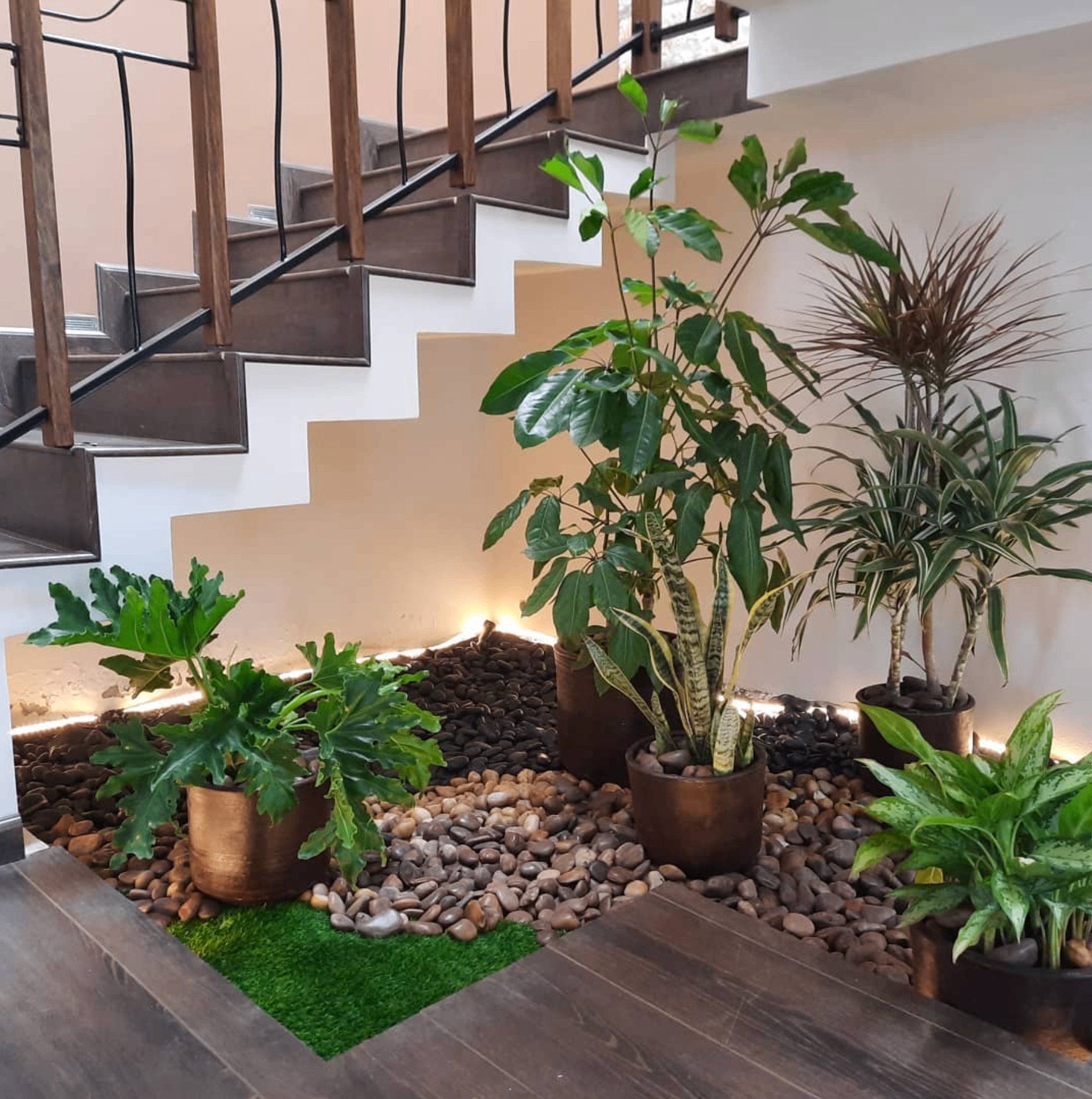 Jardín interior bajo escaleras con plantas, piedras de río e iluminación LED
